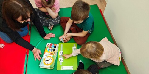 Dzieci siedzące na dywanie wybierają właściwy symbol PCS, adekwatny do tekstu w książce do czytania uczestniczącego